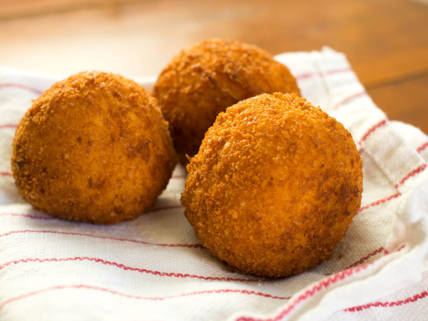 Close-up of several well-browned arancini on a patterned kitchen towel.