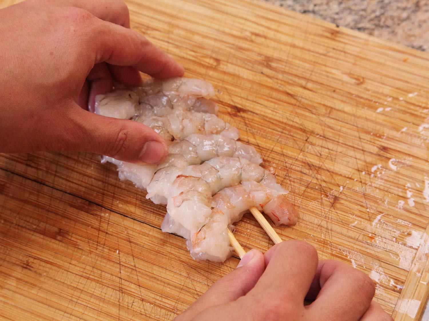 Five peeled shrimp are skewered together tightly with two bamboo skewers.