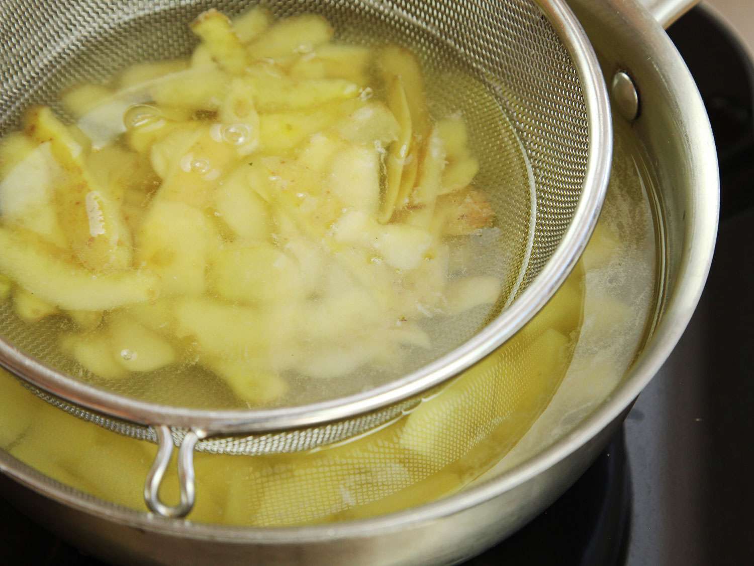 Cooking sliced peeled potatoes with the potato skins in a mesh strainer at the top of the pot. 
