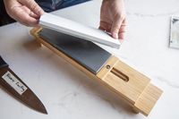 A person showing two whetstones on top of a sharpening table