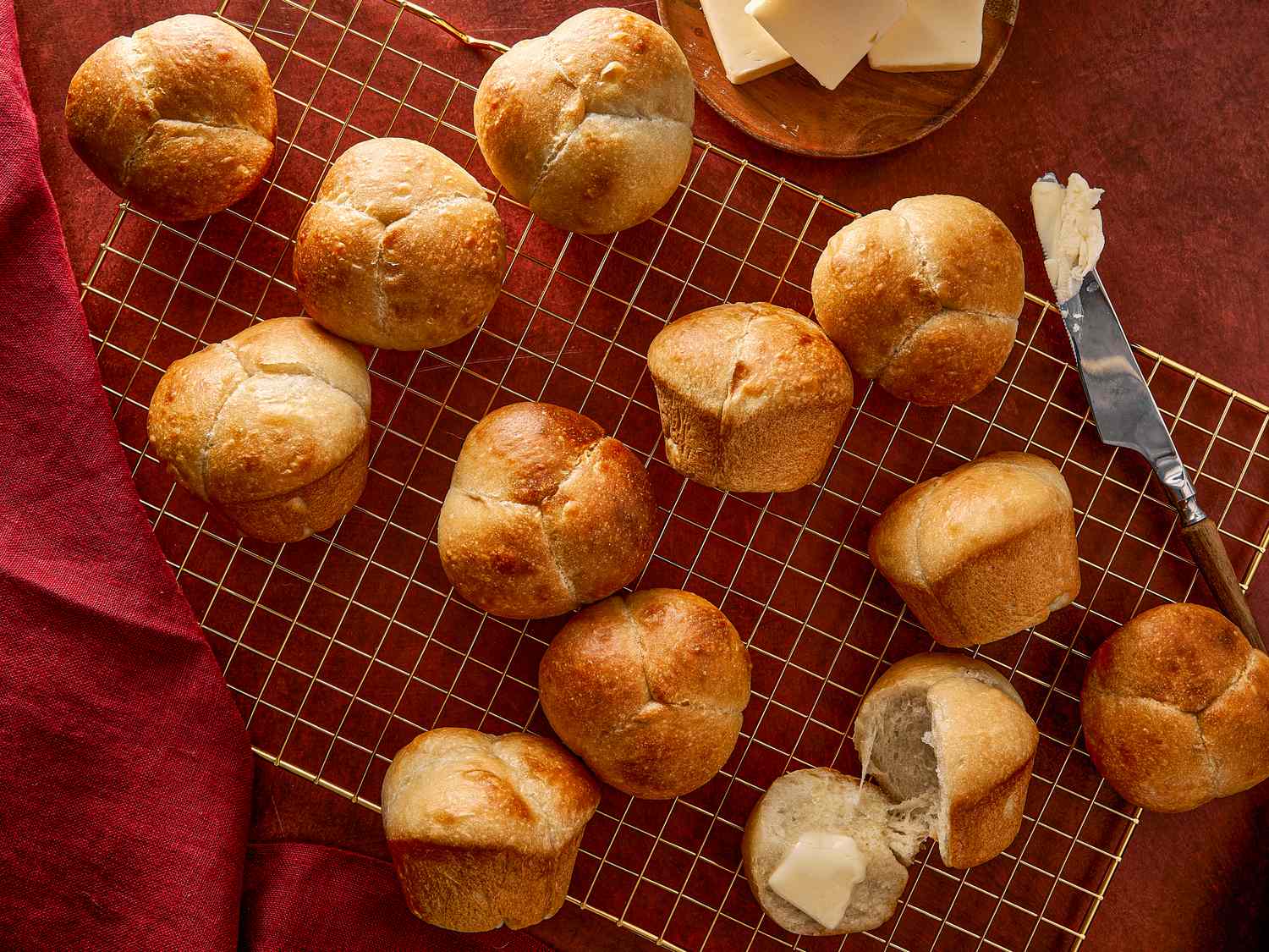 Freshly baked cloverleaf dinner rolls on a cooling rack with butter spread nearby