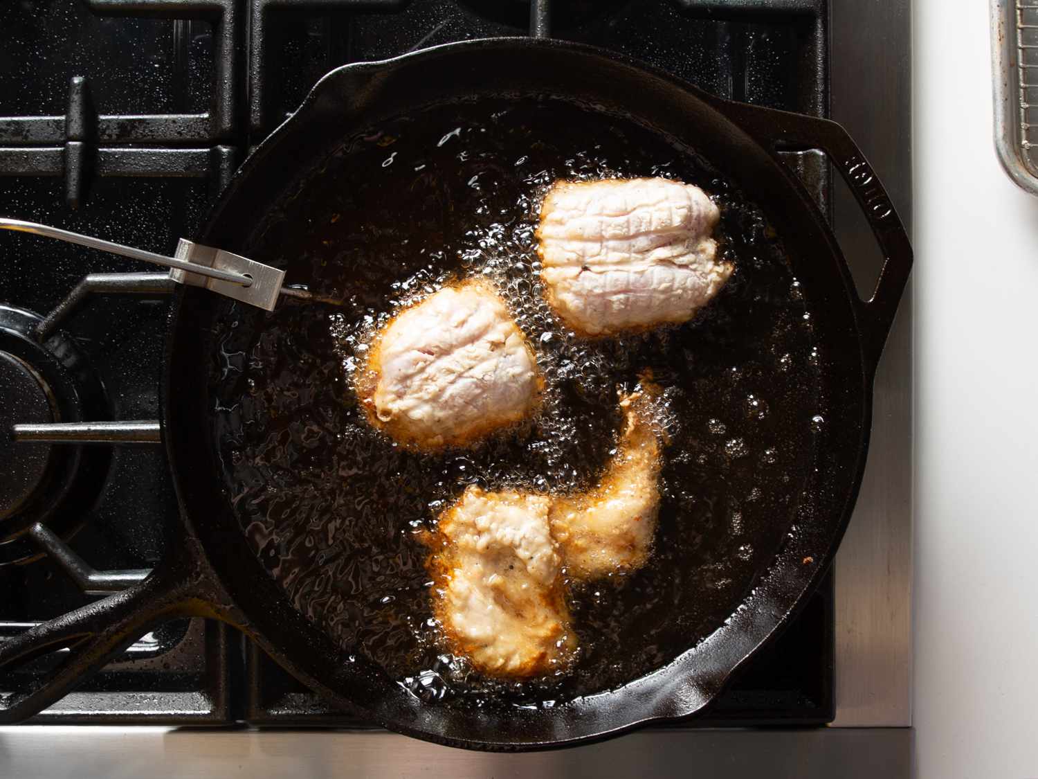  Brined and dredged chicken being fried in cast iron skillet with clip-on thermometer