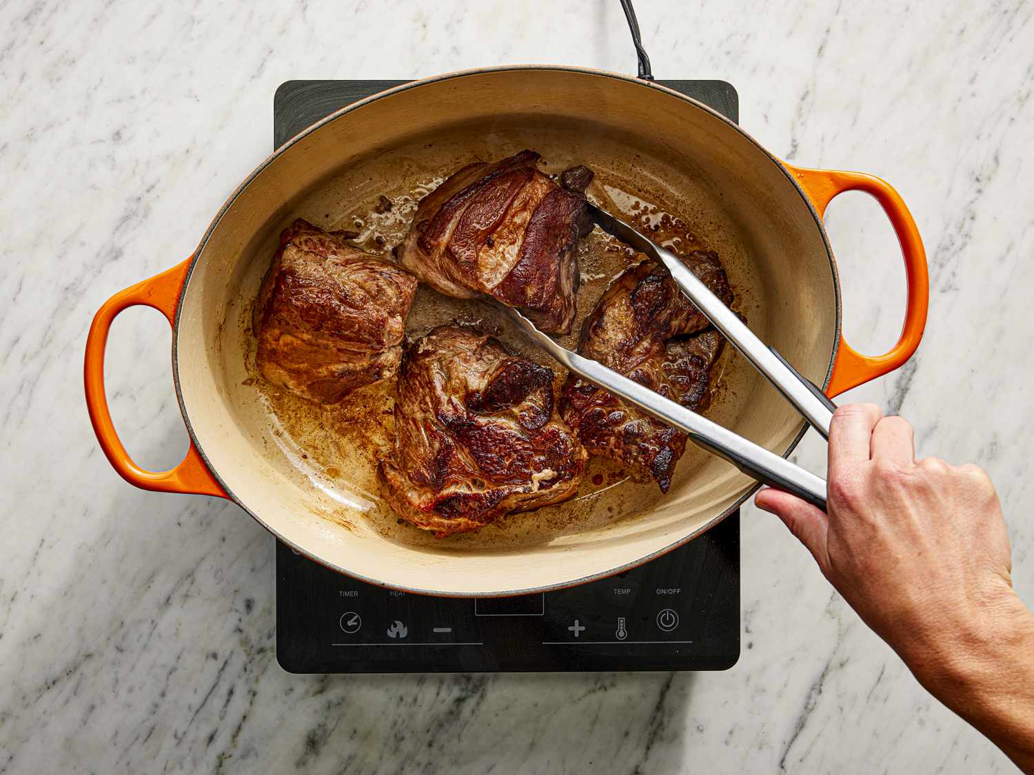Meat browning in a dutch oven being picked up with metal tongs