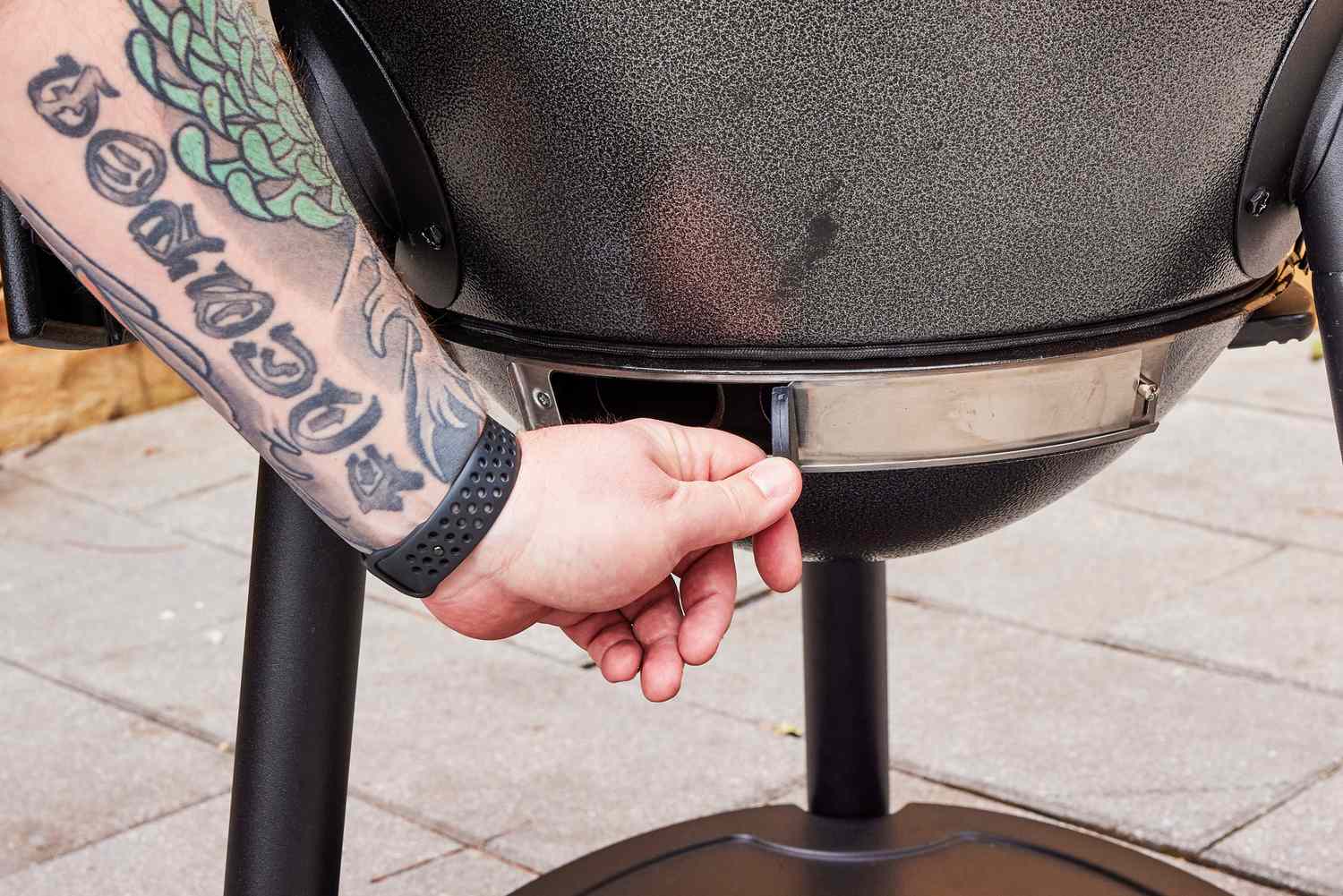 A person opens a valve on the Char-Griller E16620 Akorn Kamado Charcoal Grill