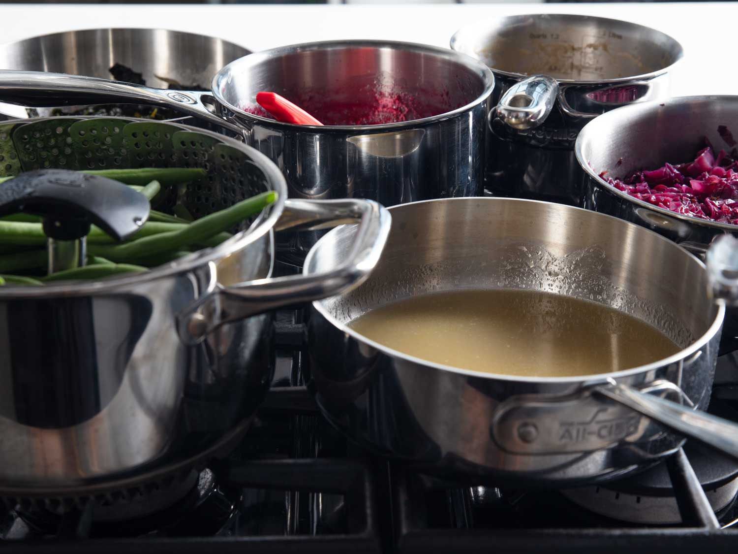 Side view of saucepans jammed up on a gas range, with many of the saucepans not directly over burners.