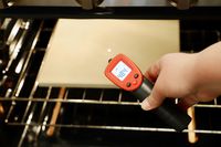 An infrared thermometer being used to take the temperature of a pizza stone in an oven.