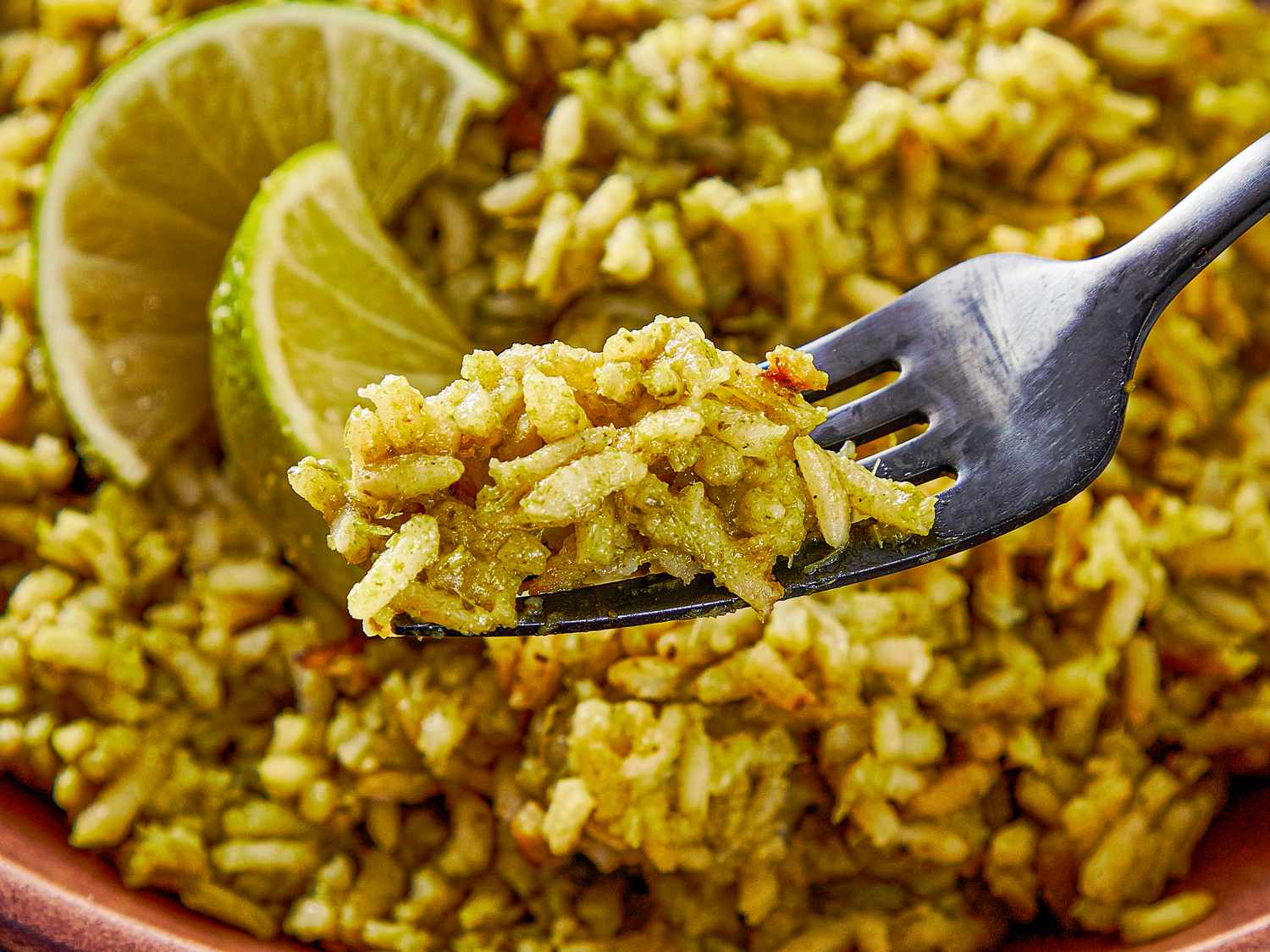 A fork holding a portion of seasoned rice with lime slices in the background