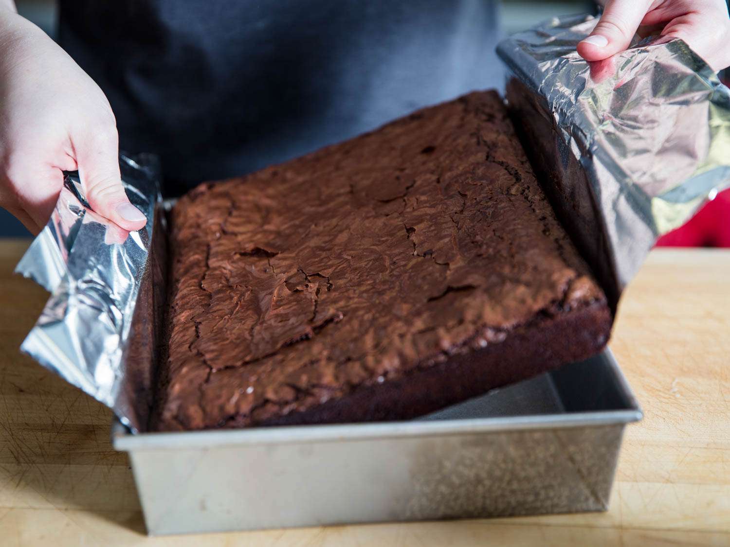 Lifting a sheet of baked brownies out of a rectangular baking pan. 