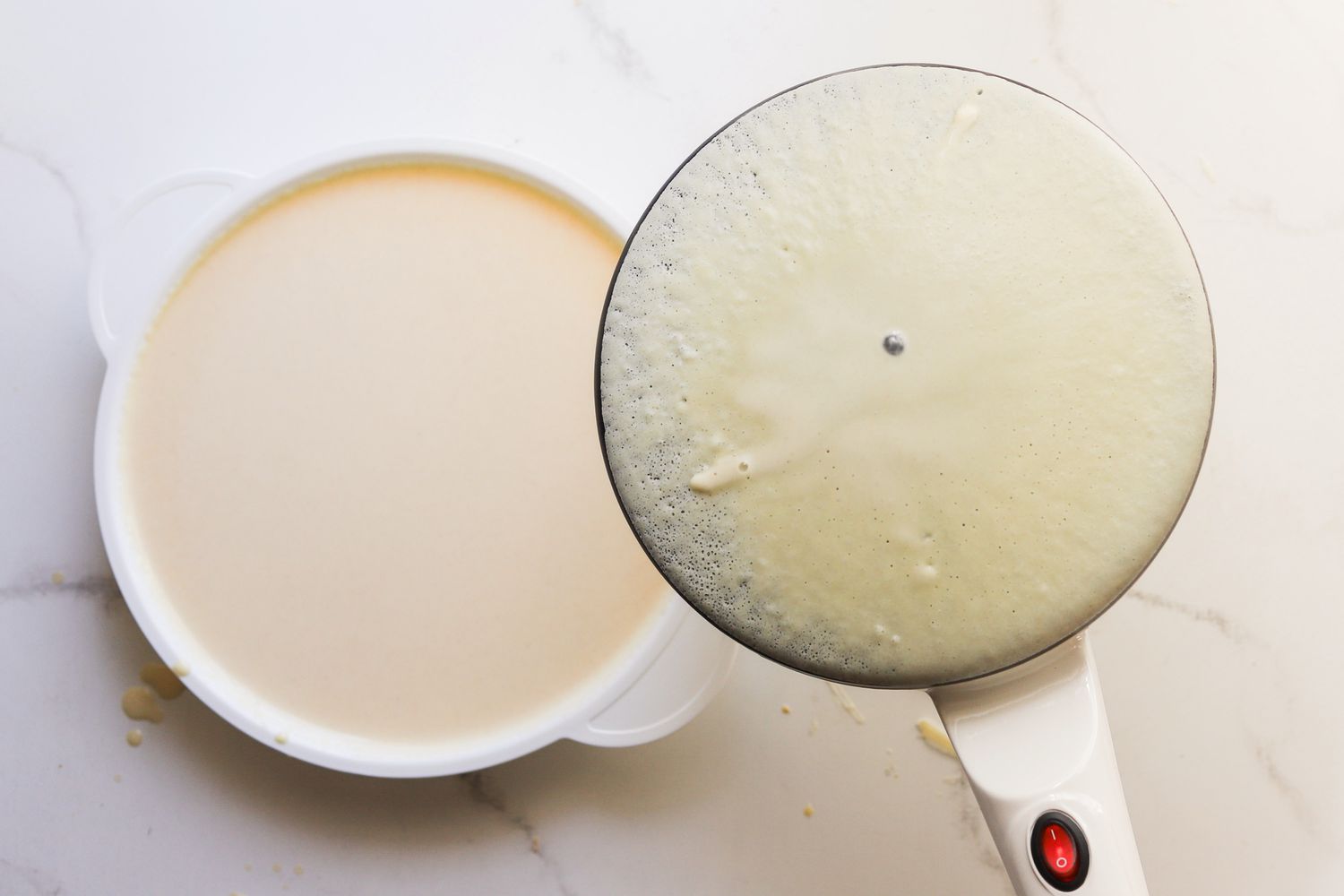 An electric crepe maker's surface being dipped into batter.
