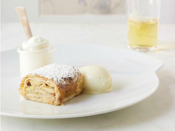 A slice of apple strudel on a plate with cream. 