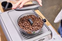 A person adds the cover onto the coffee grinder on the Breville The Barista Express Espresso Machine