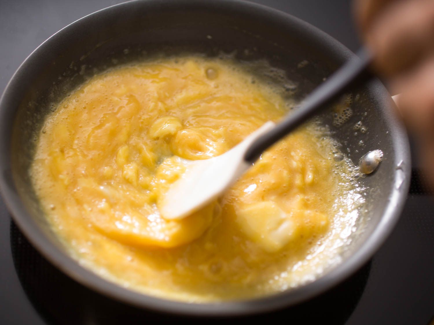 Stirring soft scrambled eggs with a silicon spatula in a non-stick skillet.