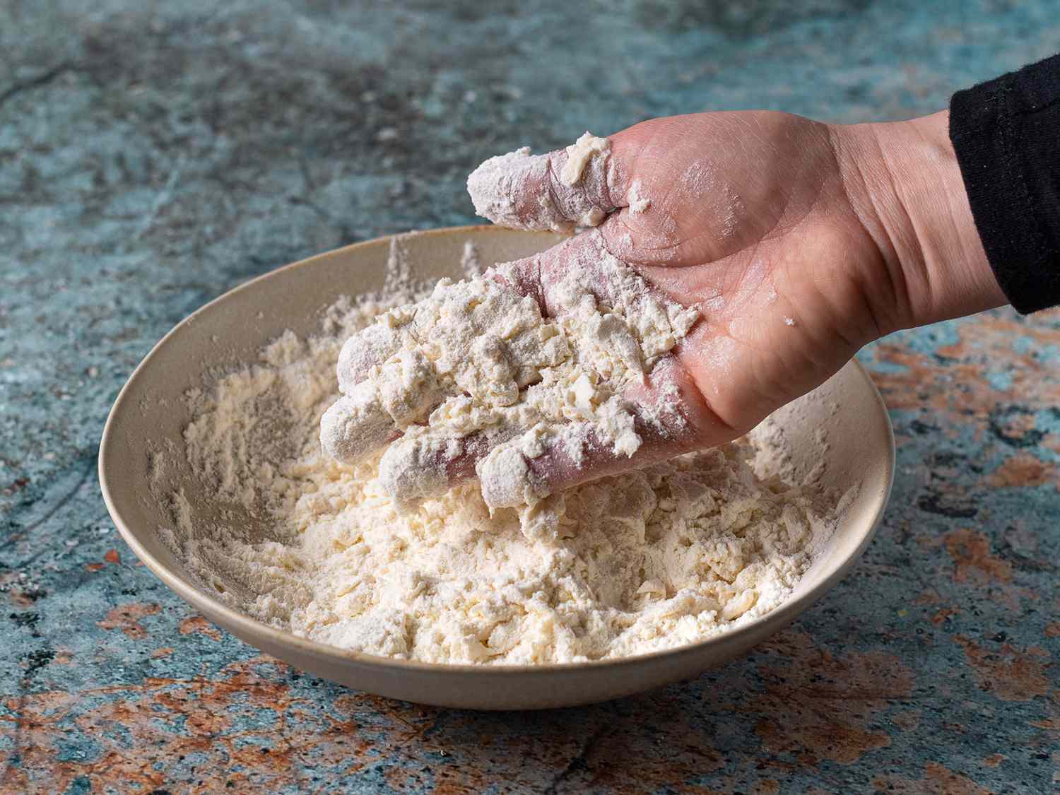 The flour with liquid worked into it, being held up by a hand to demonstrate the desired texture.