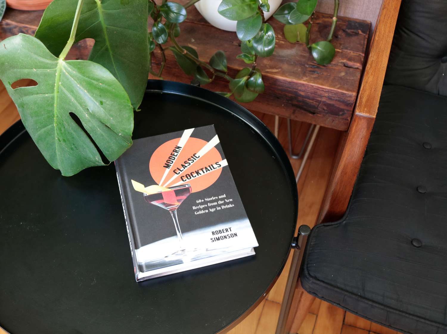 the book Modern Cocktail Classics on a black coffee table next to a chair and some plants