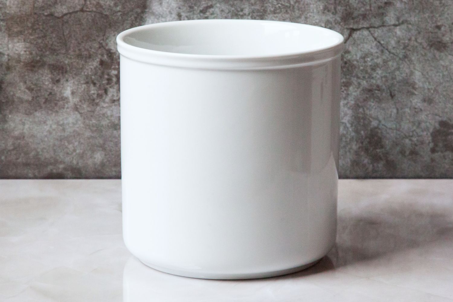 An empty white porcelain utensil crock on a white countertop