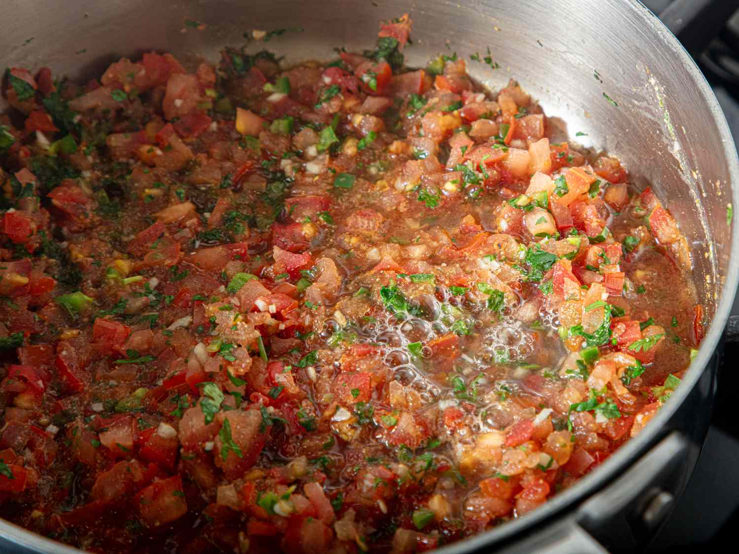 Salsa cooking with diced tomatoes herbs and garlic in a pot