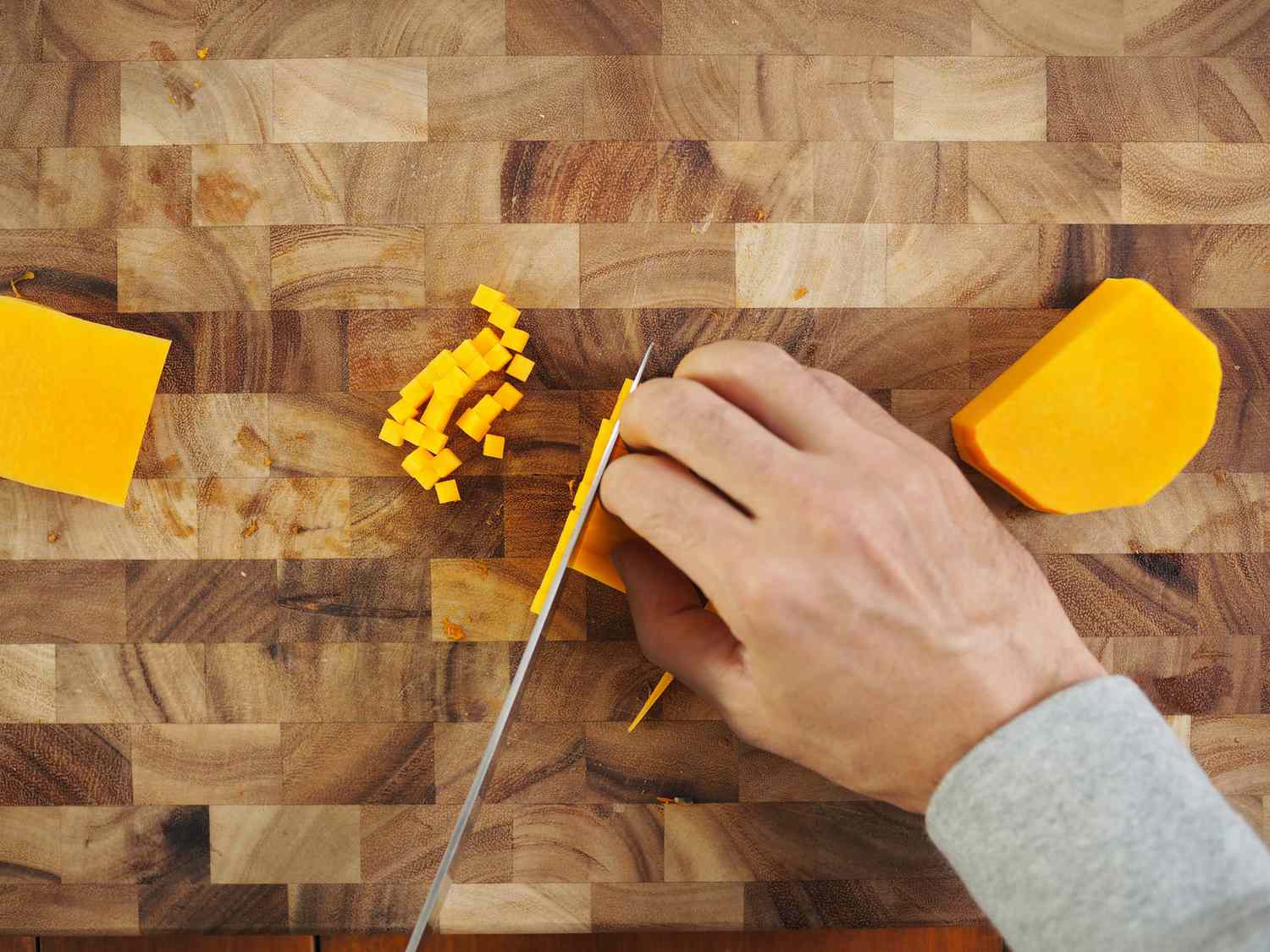 The thin strips of butternut squash being cut into small cubes.