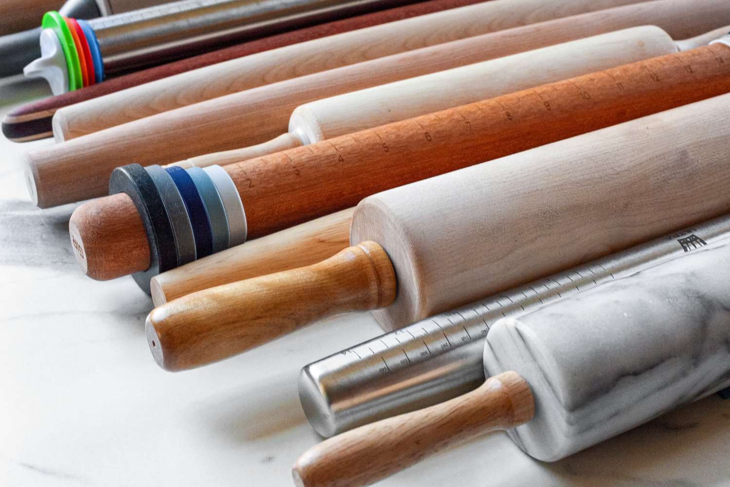 A variety of rolling pins arranged on a marble surface featuring different materials and designs