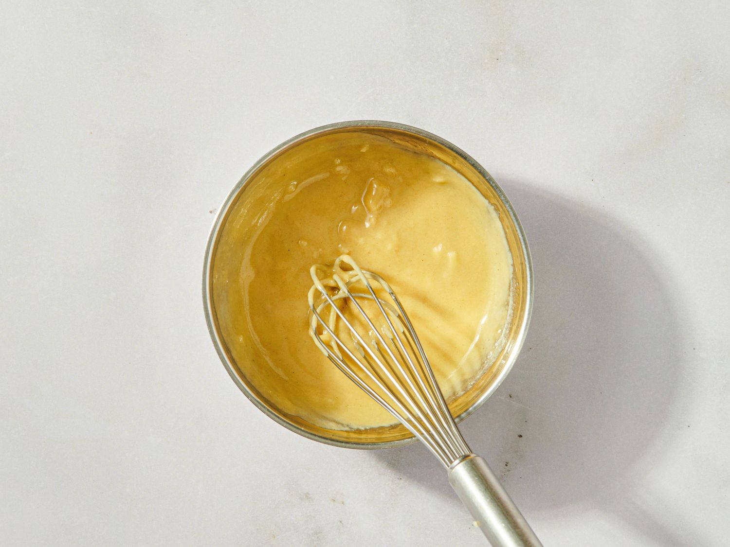 Stainless steel bowl with yellow batter and a whisk resting inside