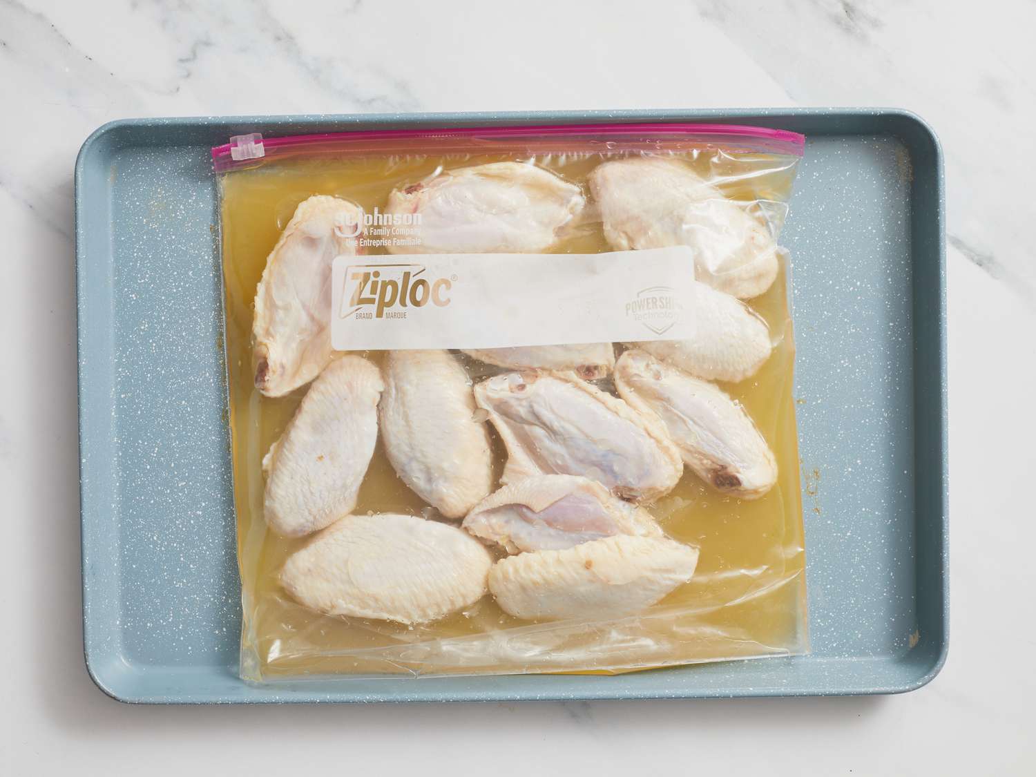 Chicken wings marinating in ziploc bag on a sheetpan