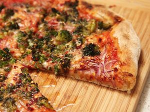 Closeup of caramelized broccoli and red onion pizza on a bamboo cutting board. A slice is missing.