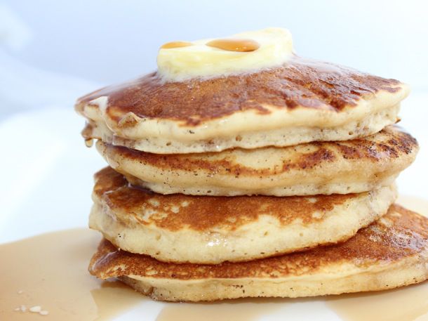 A stack of pancakes topped with butter and a drizzle of maple syrup. 