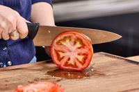A person slices a tomato using the Mercer Culinary 8-Inch Millennia Chef's Knife