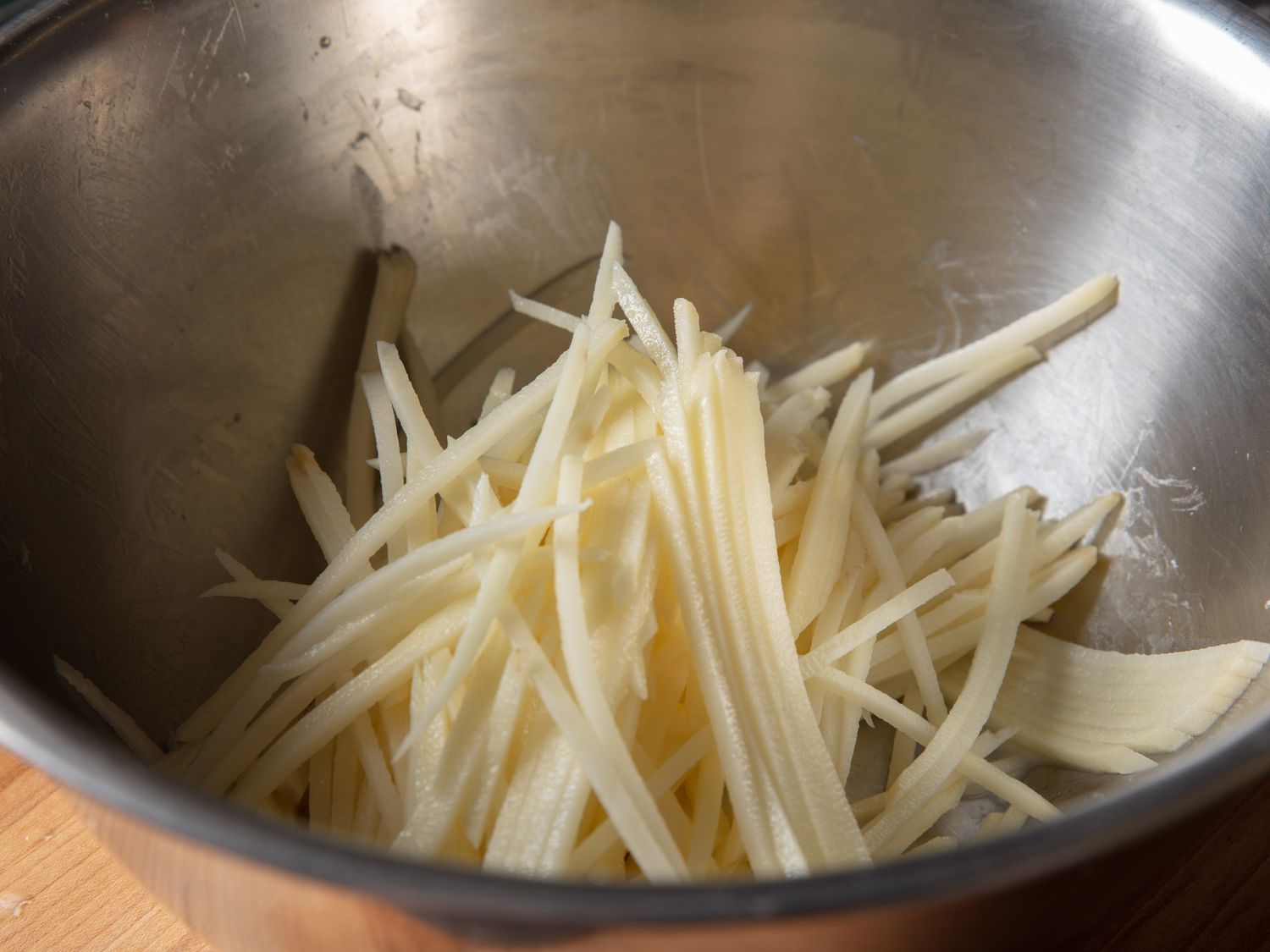 Julienned raw potatoes in a mixing bowl.