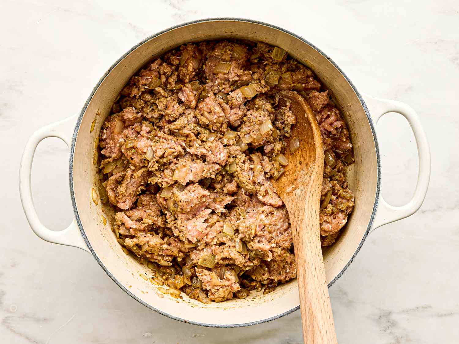 Cooking ground turkey and spices in a Dutch oven with a wooden spoon