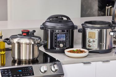 Three pressure cookers sitting on a kitchen counter with a bowl of cooked food in front of them