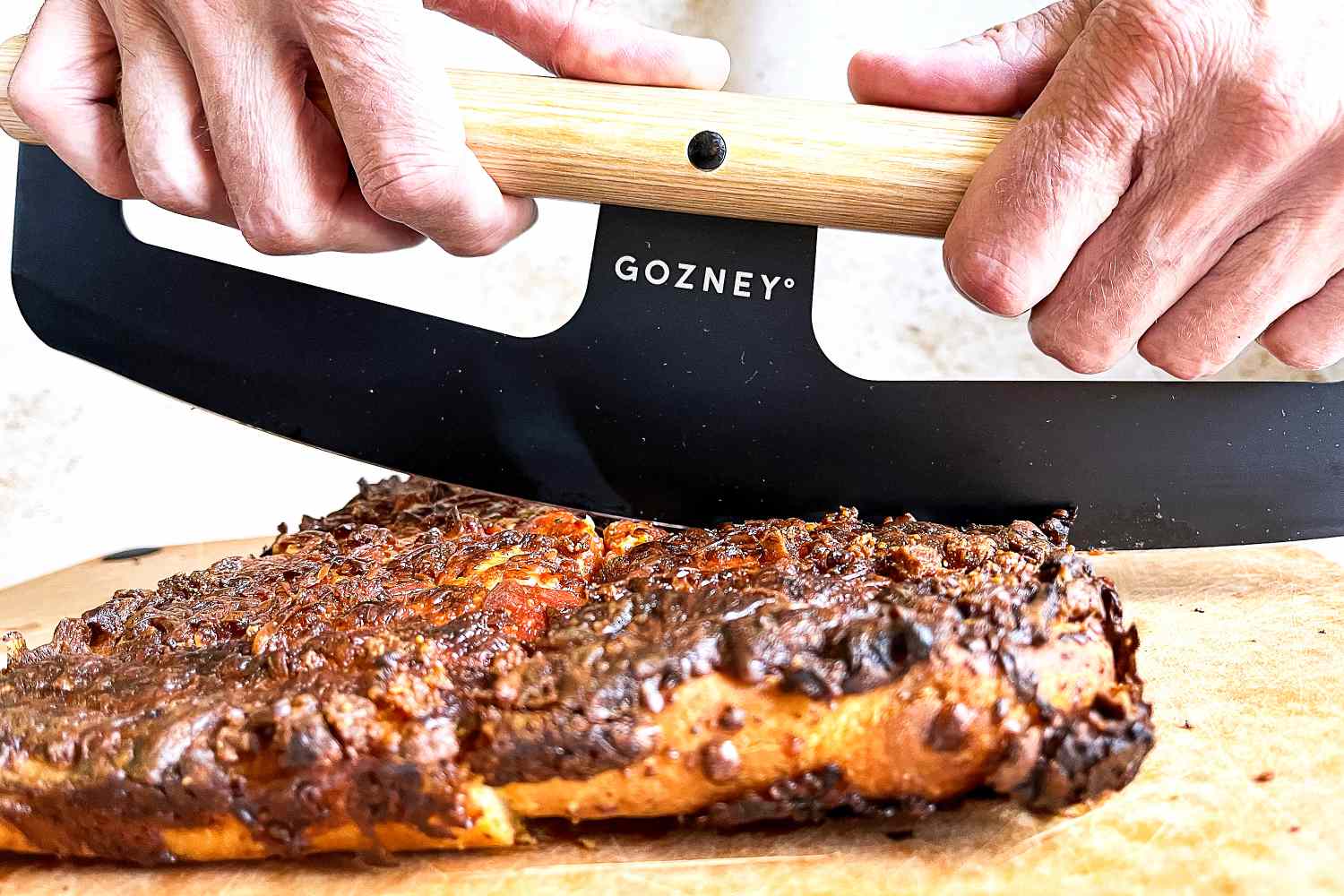 Hands using a Gozney pizza rocker to cut into a cooked food item