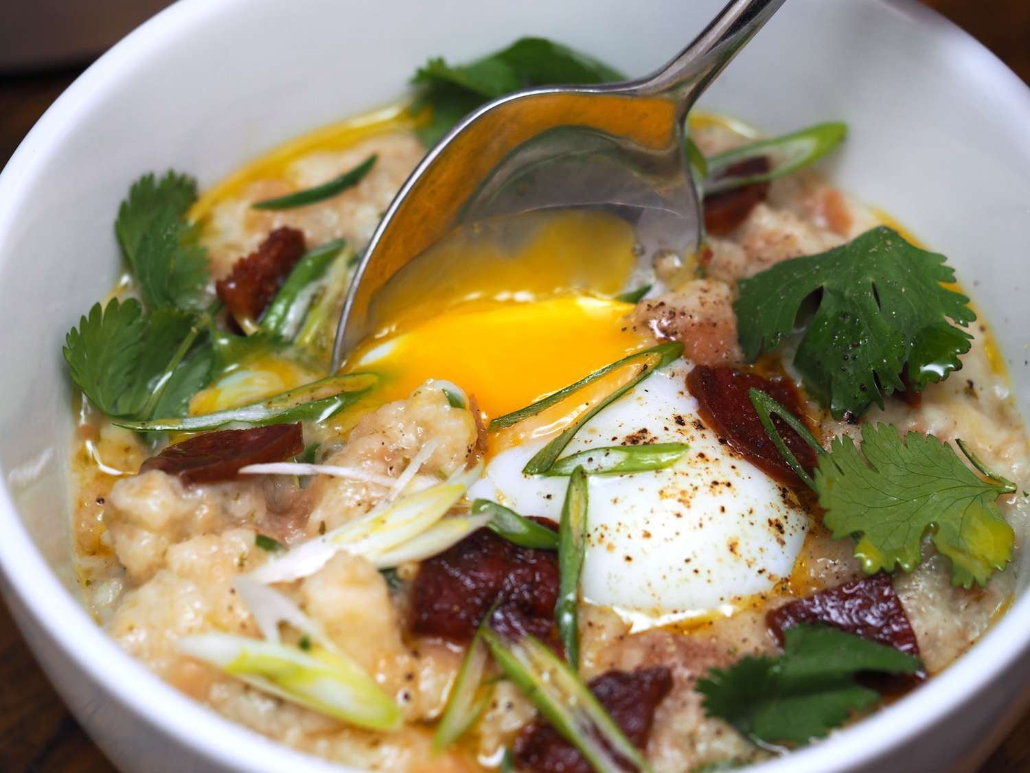 A bowl of Portuguese bread soup with a spoon inserted, breaking open the yolk of the soft poached egg in the center.