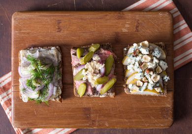 Three different Smørrebrød on a wood cutting board, each with different toppings.