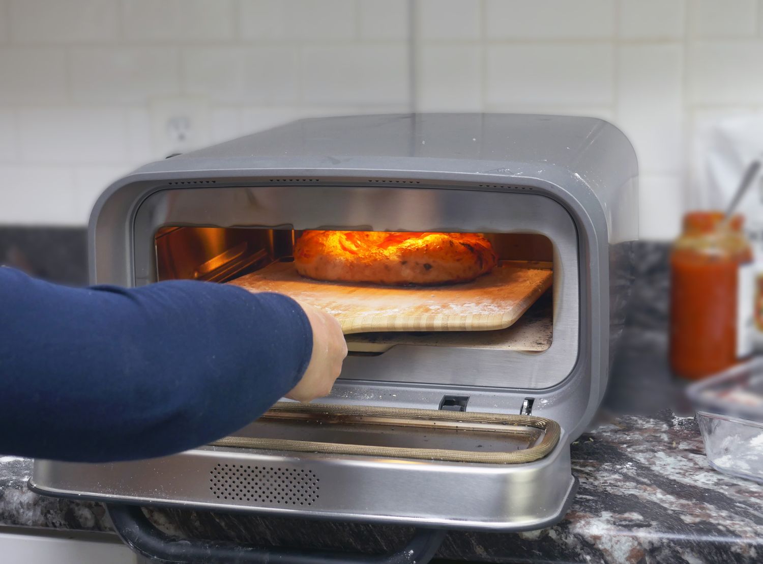 A hand placing a pizza inside an oven on a countertop