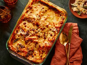 A baked lasagna in a glass dish with utensils and a napkin on the side