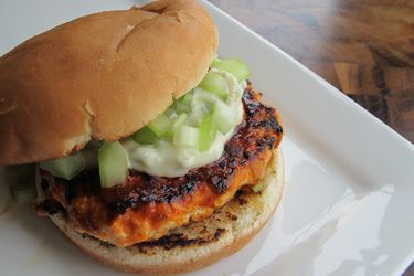 Closeup of a spicy Buffalo chicken burger, shingled slightly on a plate to show the patty and toppings.
