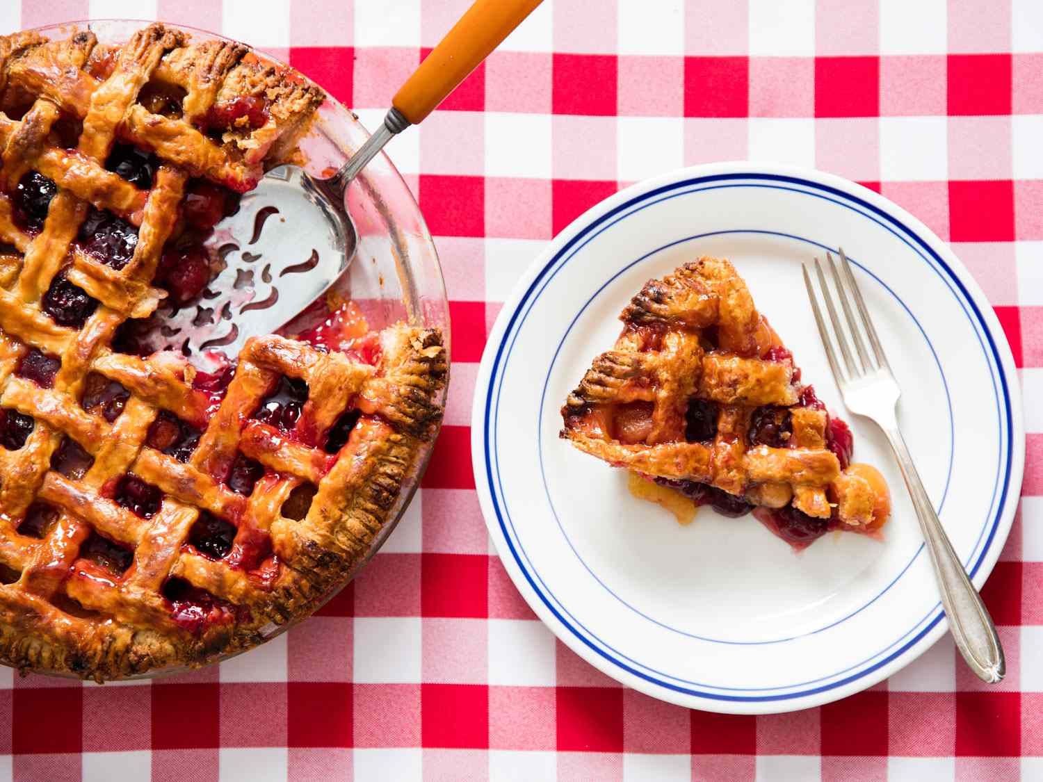 A cherry pie with a slice cut out. The slice is on a plate next to the pie dish. 