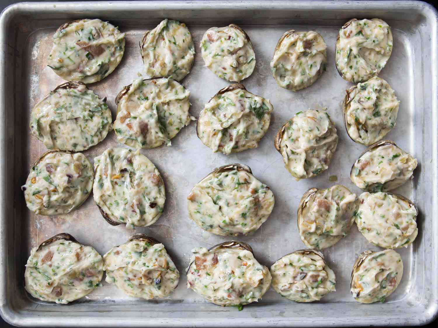 Clams in half-shell topped with compound butter on rimmed baking sheet