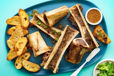 Overhead view of roasted bone marrow on a plate with toasted baguettes mustard and parsely 