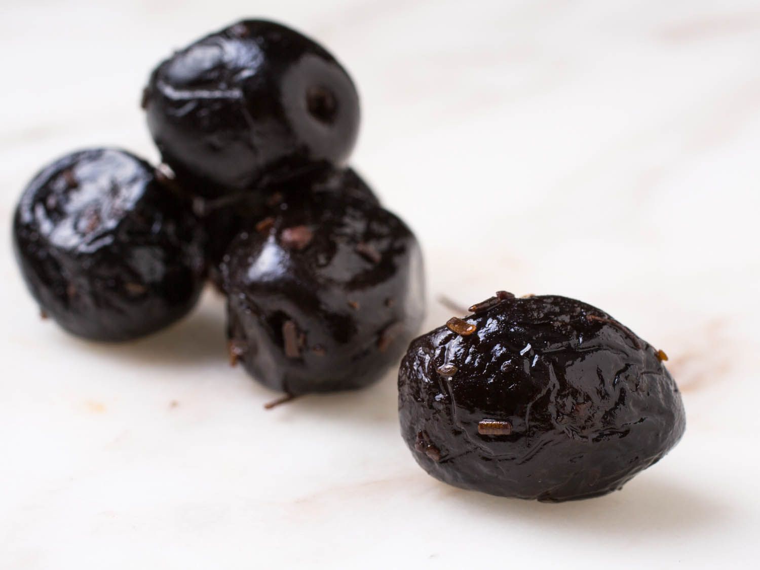 Closeup of shiny, wrinkled black olives on marble countertop