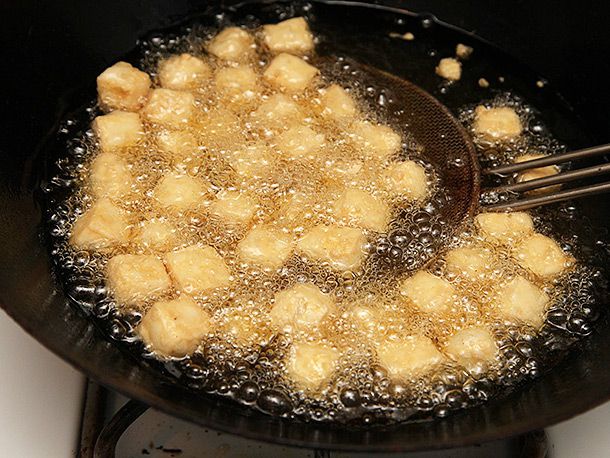 Deep-frying thinly-battered tofu in a wok for vegan kung pao tofu