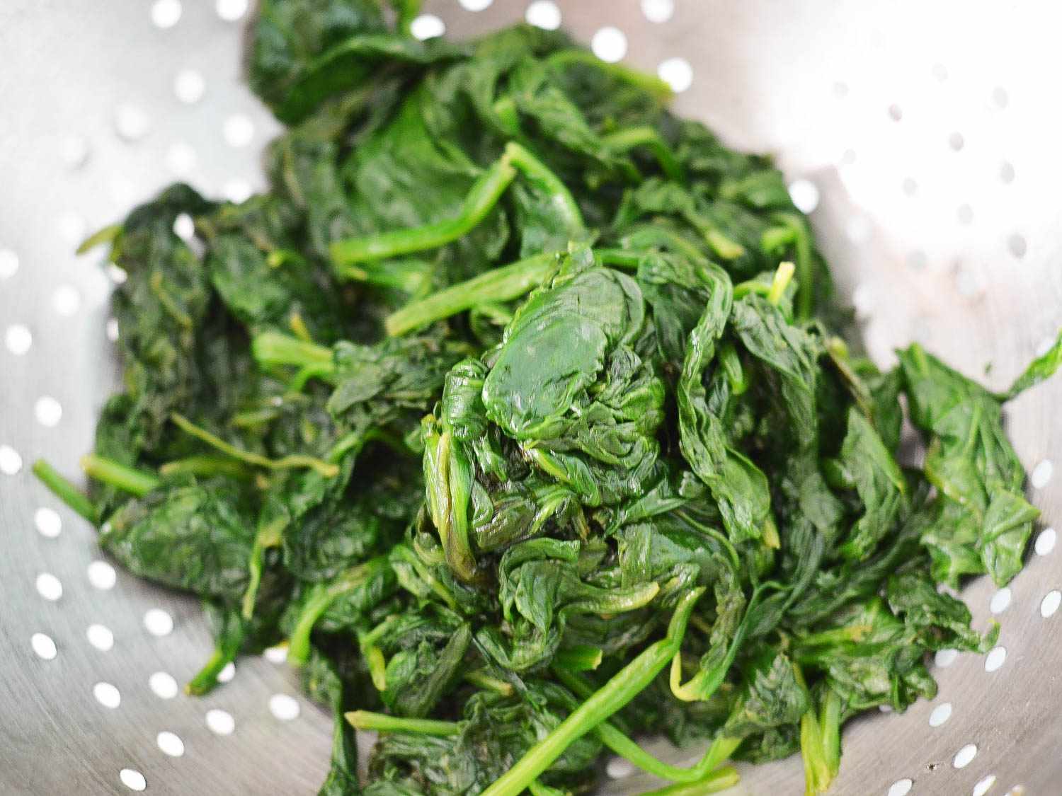 Draining cooked spinach in a colander to remove moisture.