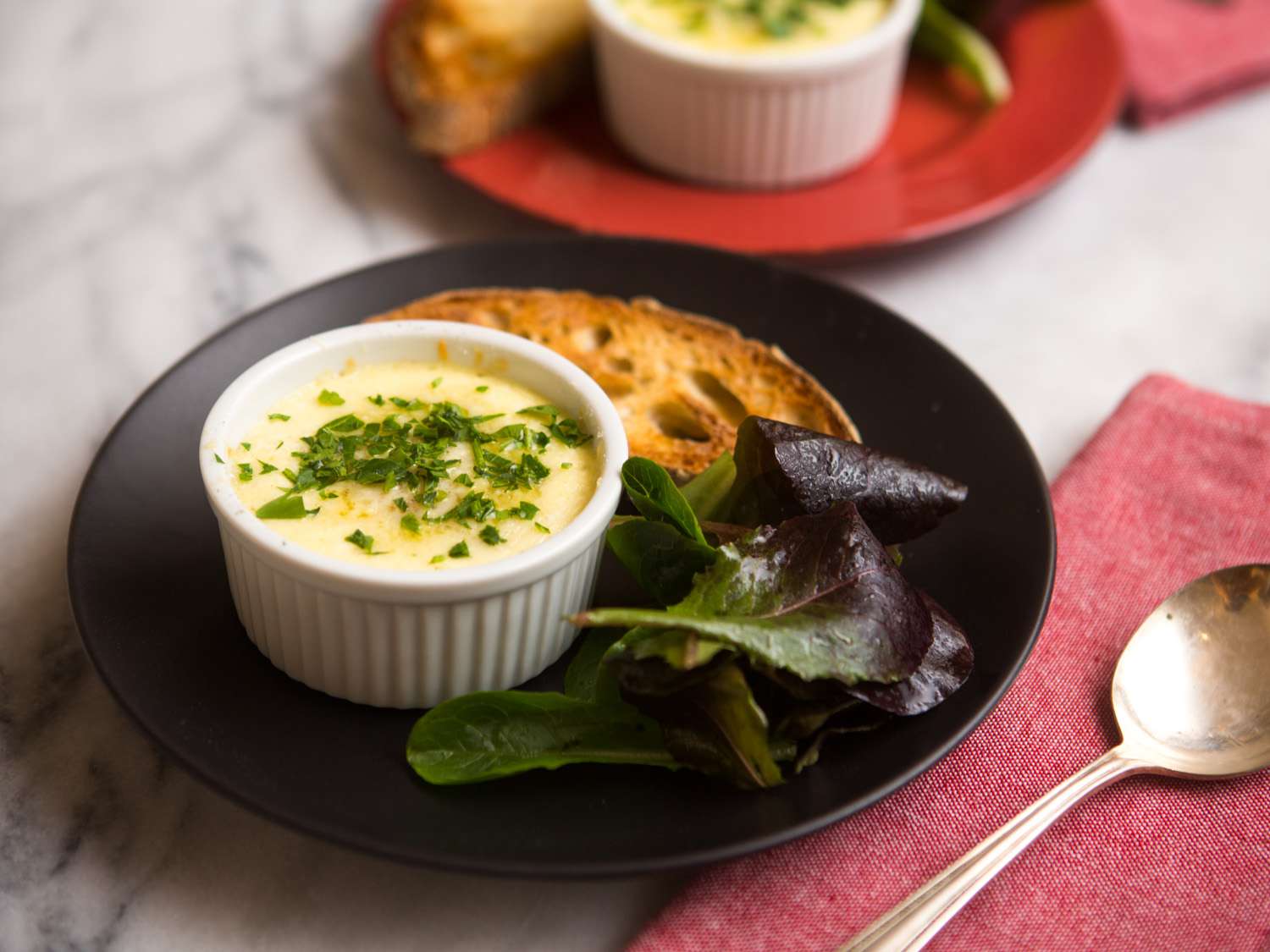 Mushroom and Gruyère eggs en cocotte, served with small toasts and greens on a black plate.