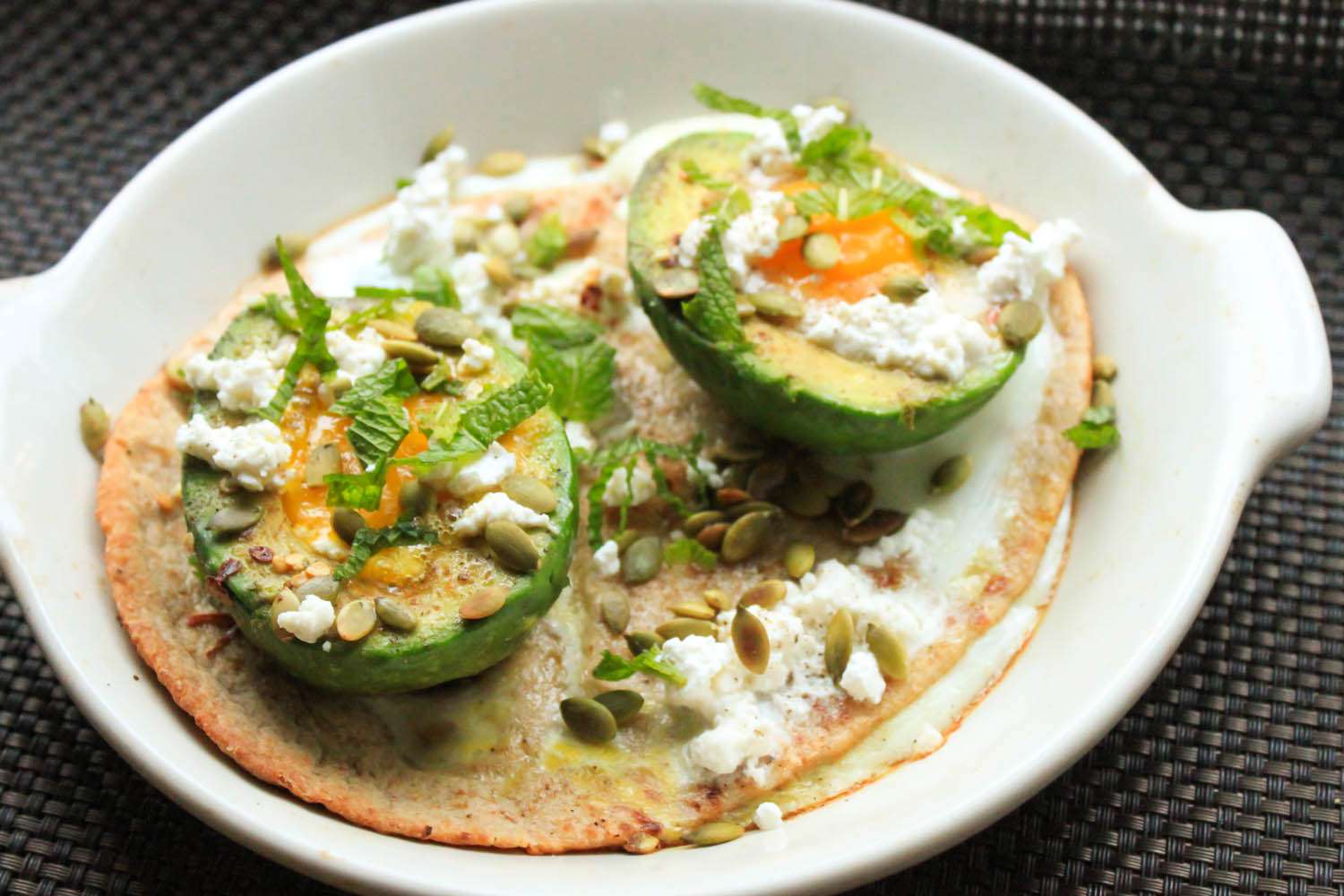 A plate of vegetarian baked eggs in avocado cups with mint and feta.