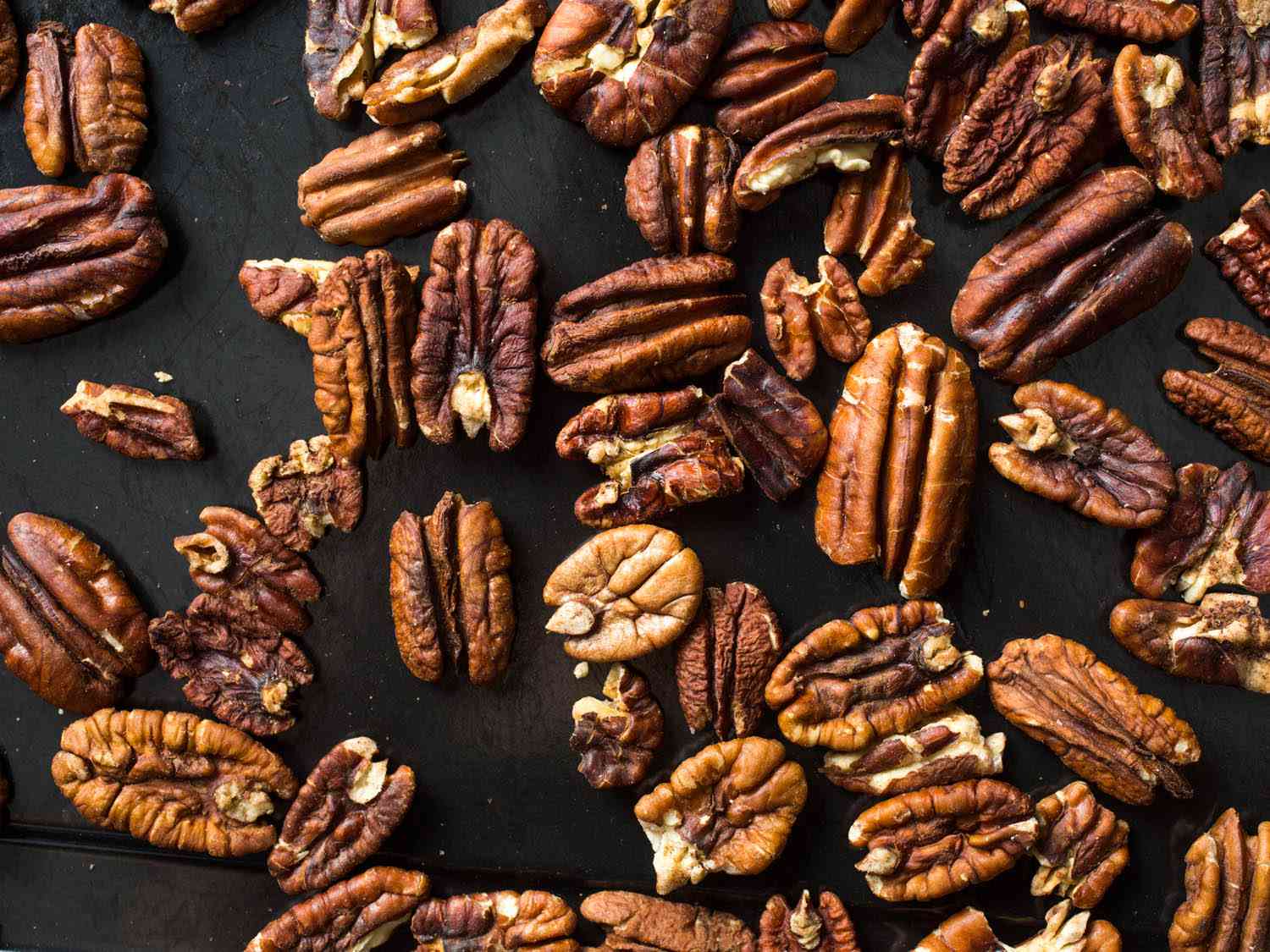 Overhead shot of raw pecan halves on a black background.