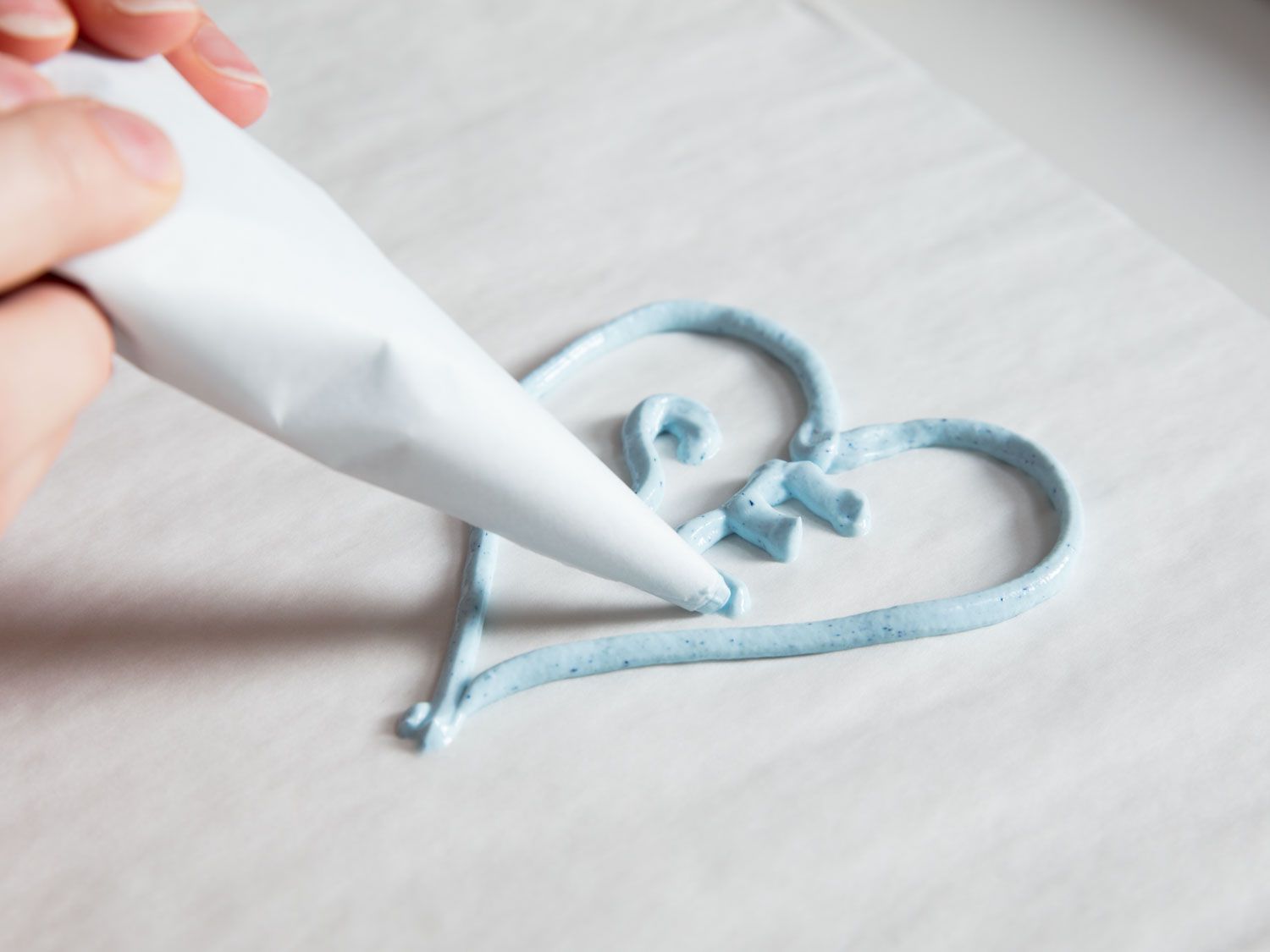 Two hands using a parchment paper piping bag to make a heart-shaped design.