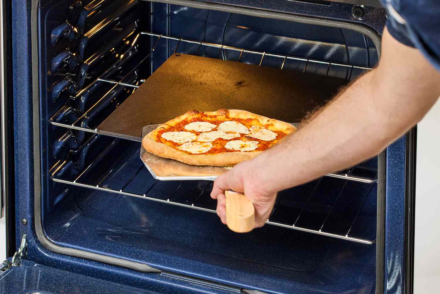 A person retrieving a cooked pizza using a pizza peel.