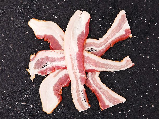 A "double X" arrangement of raw bacon slices on a plastic cutting board.