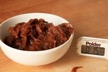 A bowl of dark brown caramelized onions next to a timer set to 15 minutes.