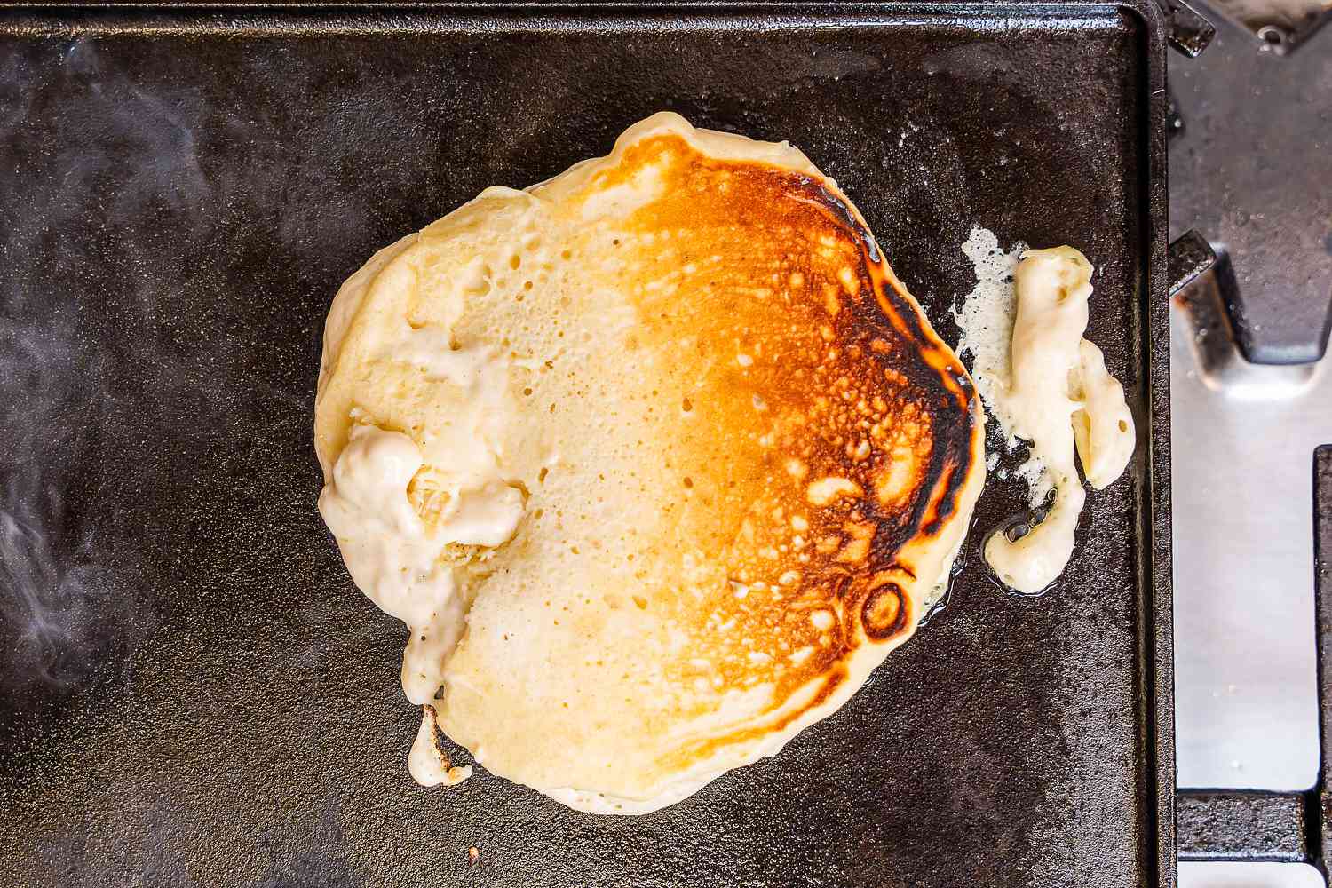 An unevenly cooked pancaked on an electric griddle